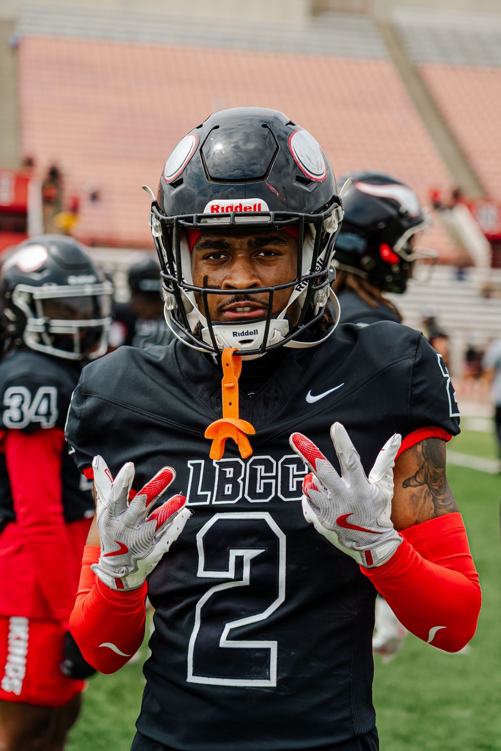 Football players in black jerseys and red pants show hand signals during practice on the field.