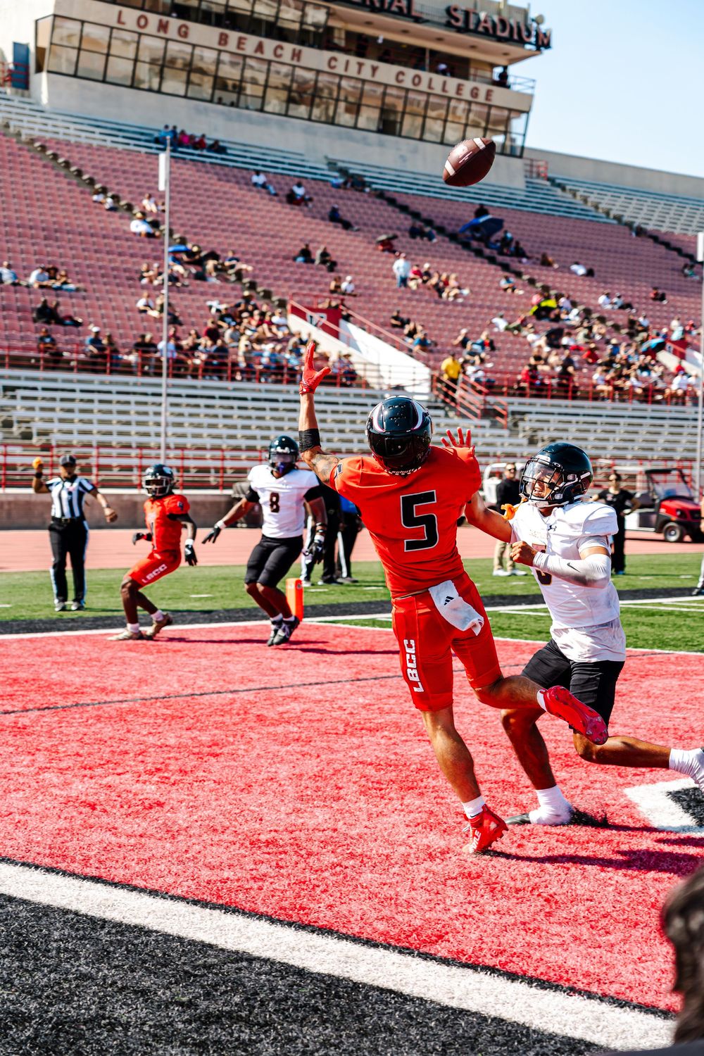 Football player dives for a touchdown in an empty stadium while being tackled by defenders in red uniforms.
