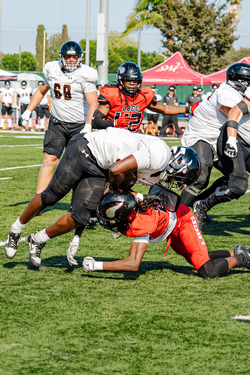 Football players dive and tackle during an intense play on a sunny grass field during a game.