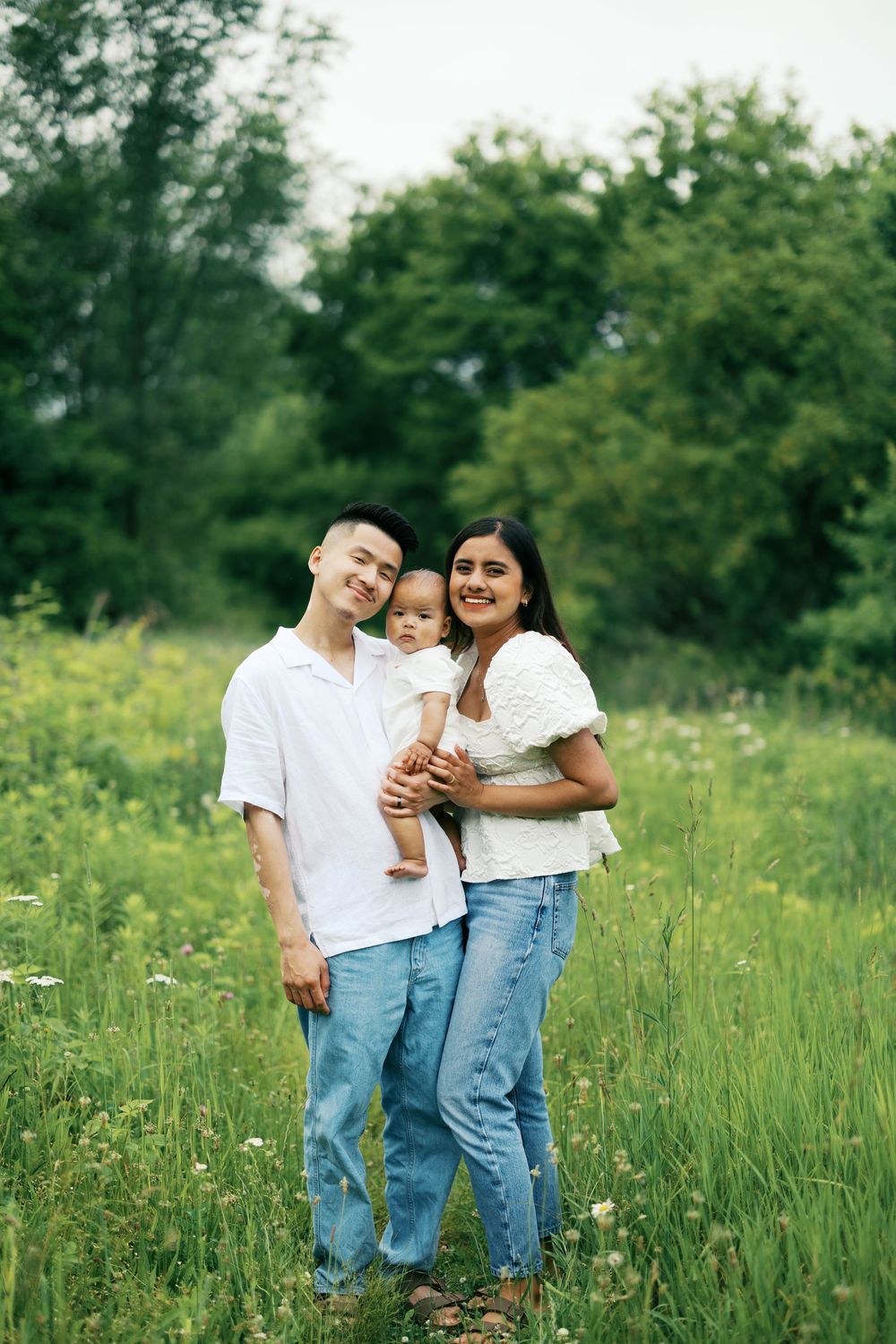 Family wearing white shirts and blue jeans share joyful moments together in a blooming wildflower meadow on a sunny day.