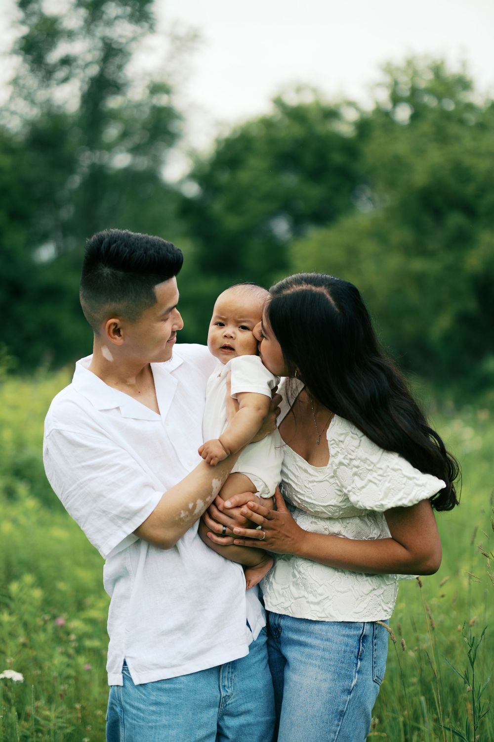 A family enjoys tender moments together in a grassy meadow while wearing casual white and blue outfits.