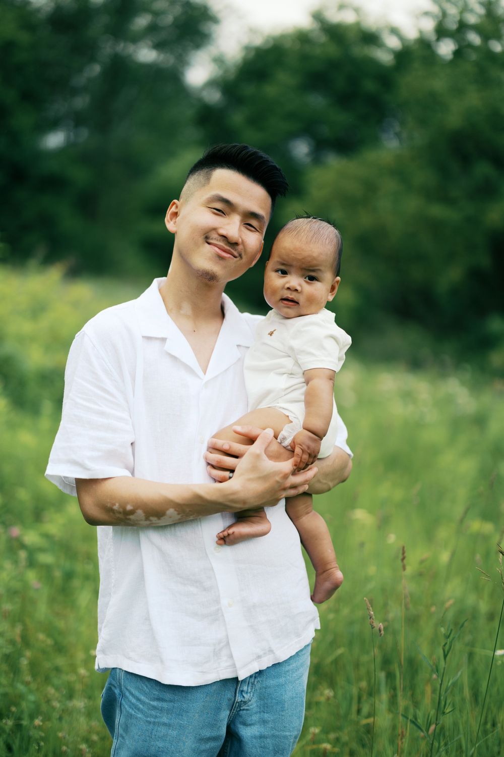 A heartwarming portrait of a parent and baby standing together in a grassy field on a sunny day.
