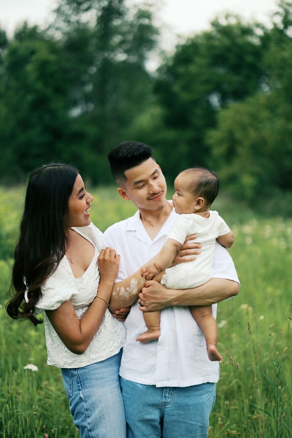 A family shares tender moments together in a sunlit meadow wearing coordinated white tops and blue jeans.