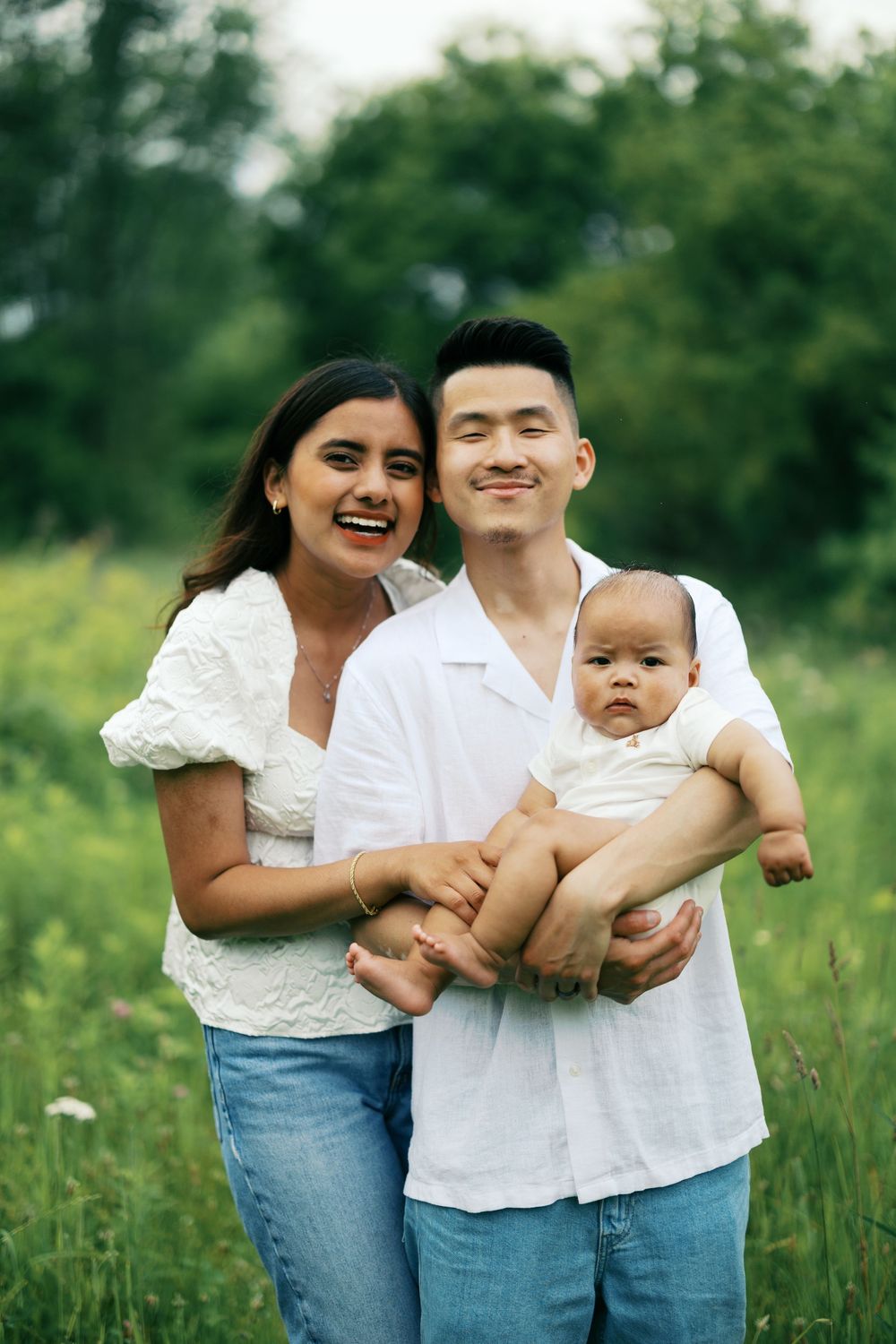 A family wearing white tops and jeans shares joyful moments together outdoors in a green summer meadow.