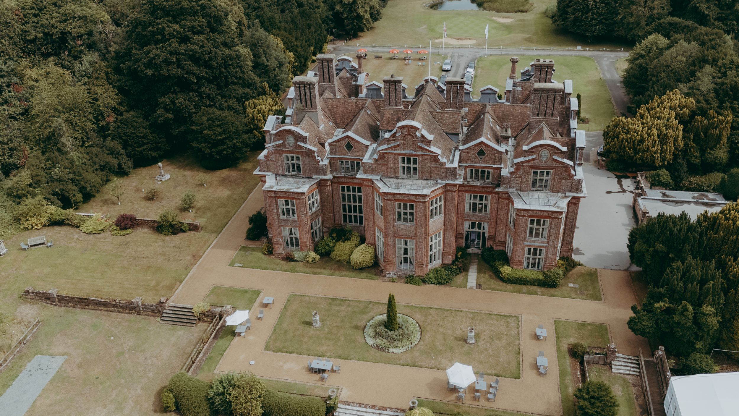 Aerial view of a grand Victorian-style mansion with Tudor architecture surrounded by manicured grounds.