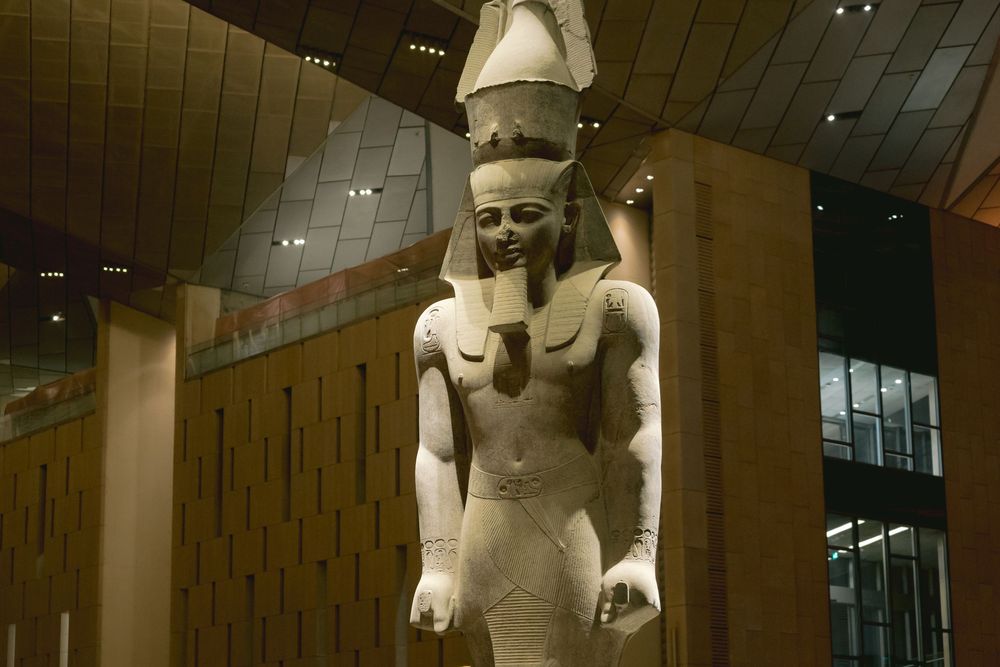 Ancient Egyptian statue of a seated scribe displayed in a museum with warm lighting and dark background.
