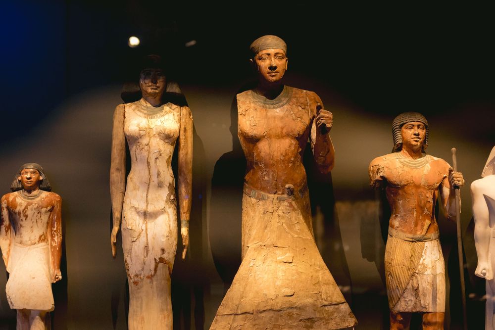 Collection of ancient Egyptian statues displayed in a museum with dramatic lighting.