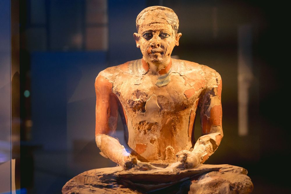 Ancient Egyptian limestone statues of seated scribes arranged in a museum display case.