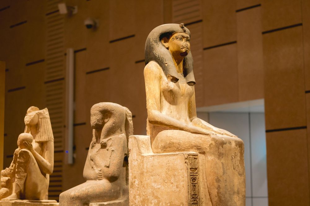 Ancient Egyptian limestone statue of a seated figure displayed in a museum setting.