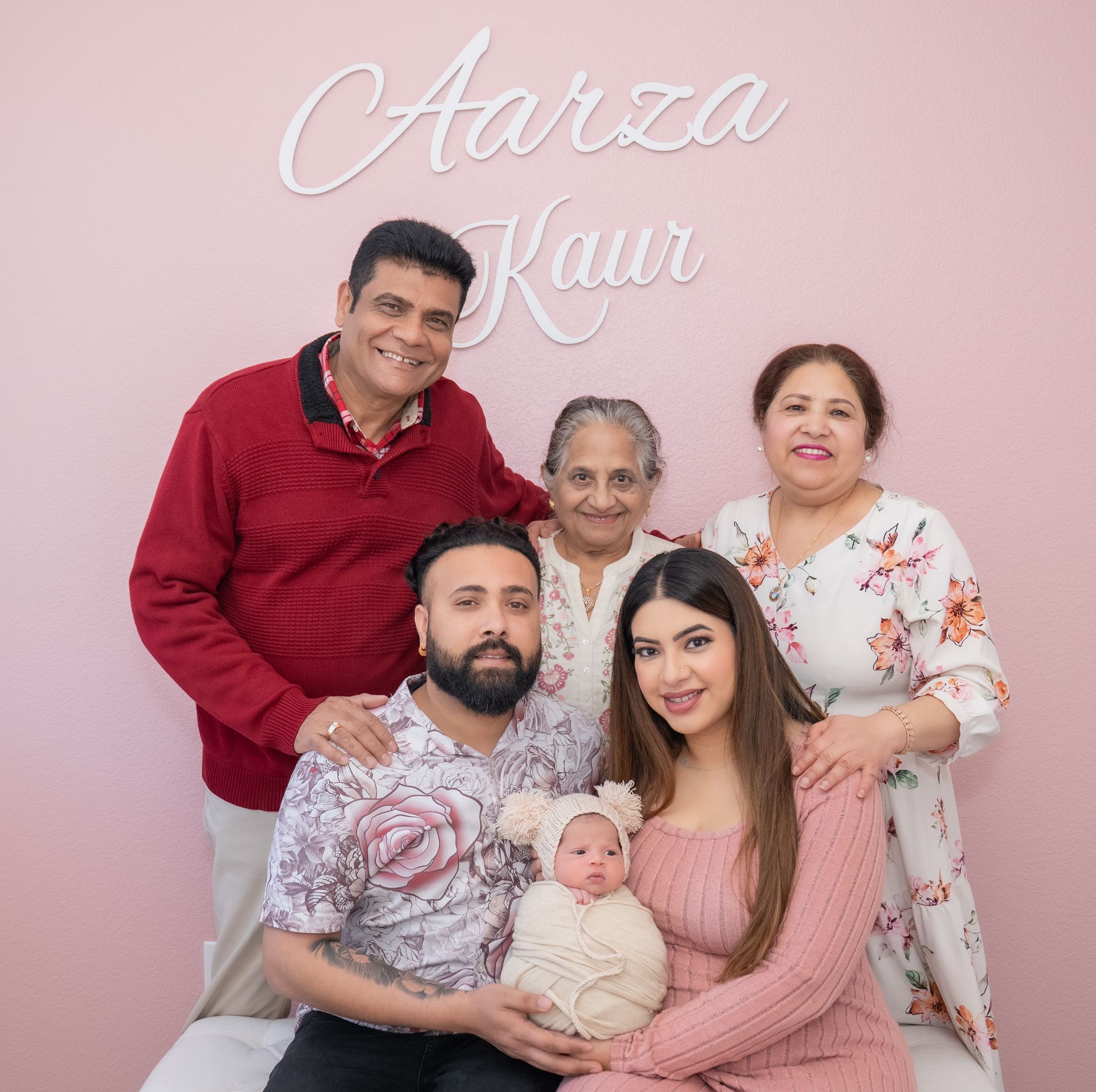 Family photo session in a pink studio with people wearing coordinating red and white outfits during a portrait shoot.