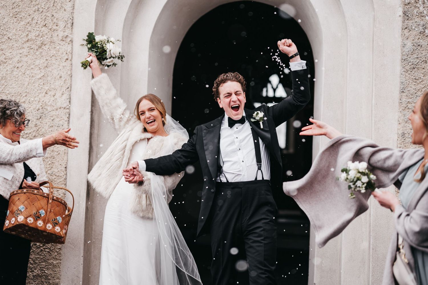 A joyful couple exits a church doorway while guests toss confetti and rice during their wedding celebration.
