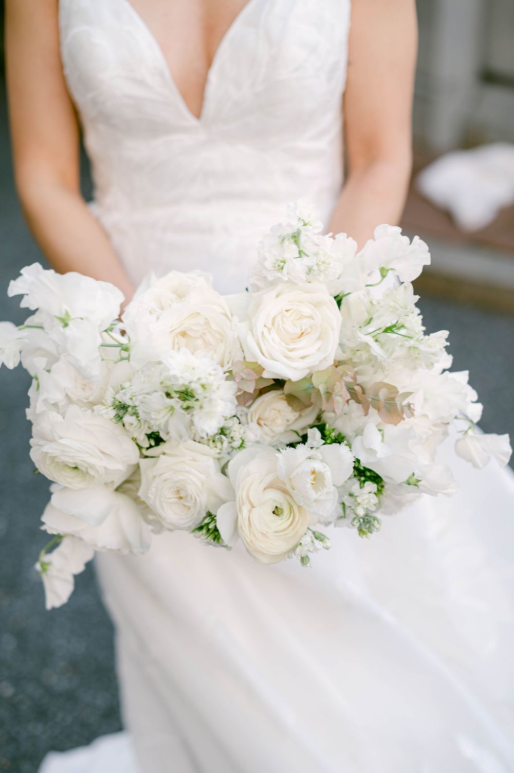 Pure white wedding bouquet featuring roses and delicate flowers against bridal gown.