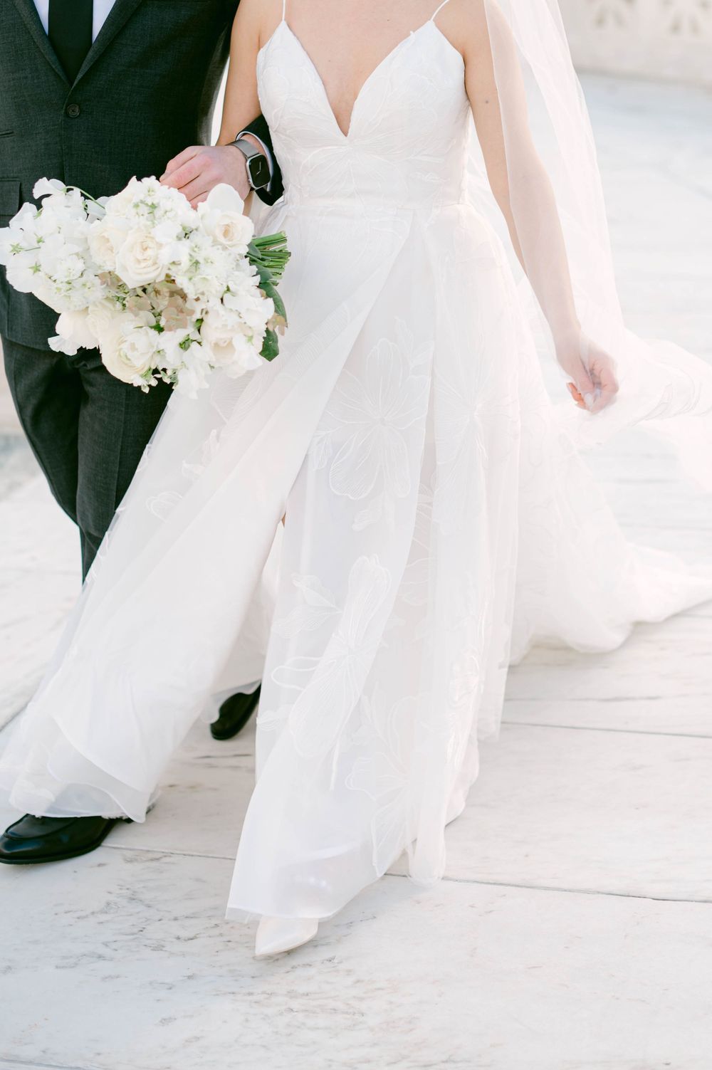 Wedding dress detail showing a white flowing gown with plunging neckline and elegant white floral bouquet.