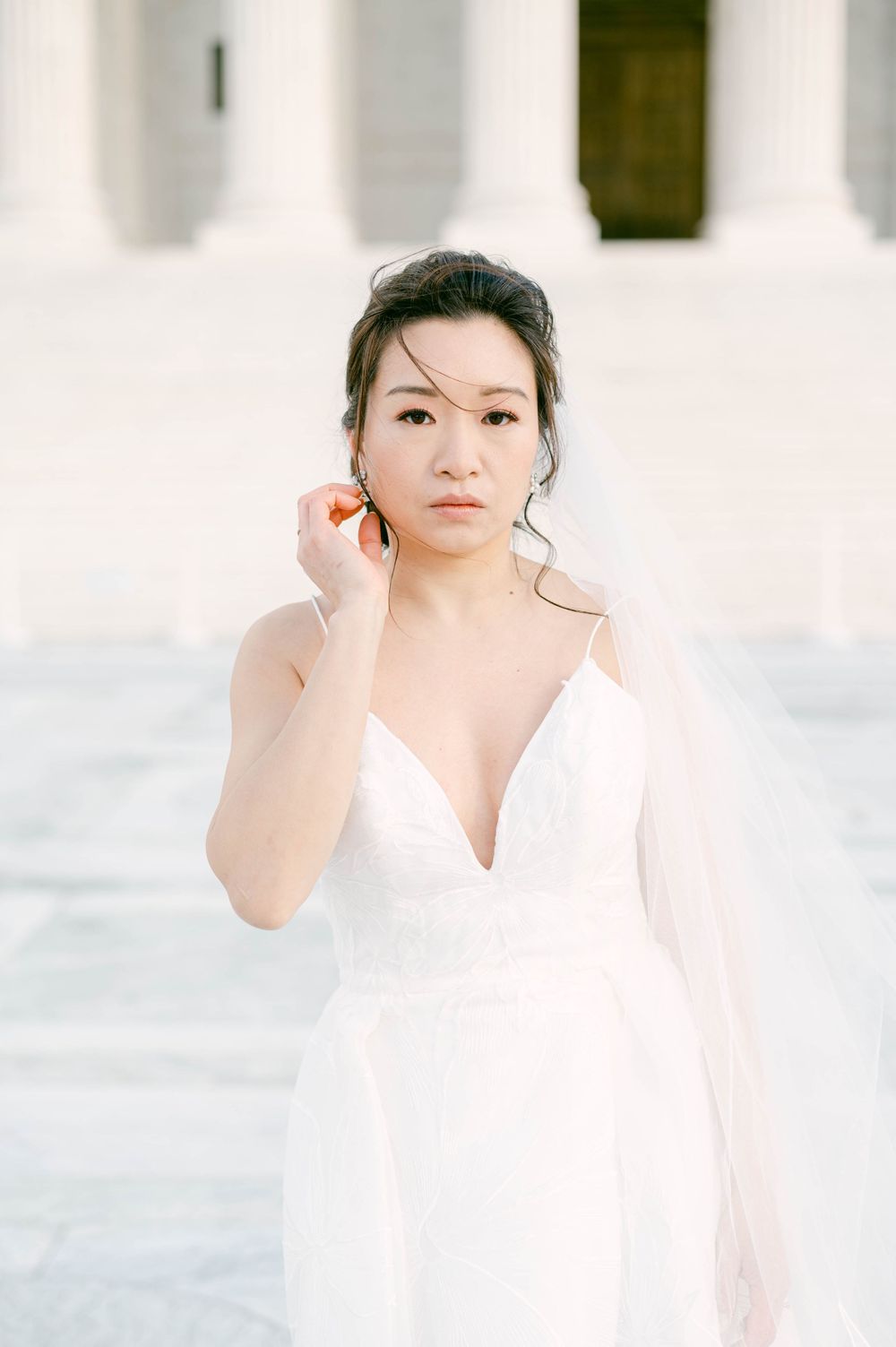 Elegant bride in a white plunging neckline wedding dress against white architectural backdrop.