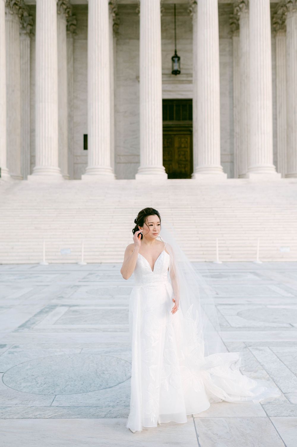 Bride in flowing white dress posing on steps of neoclassical building with columns.