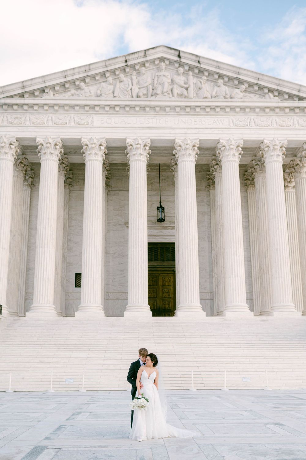 Wedding couple embracing in front of Supreme Court building with classical columns.