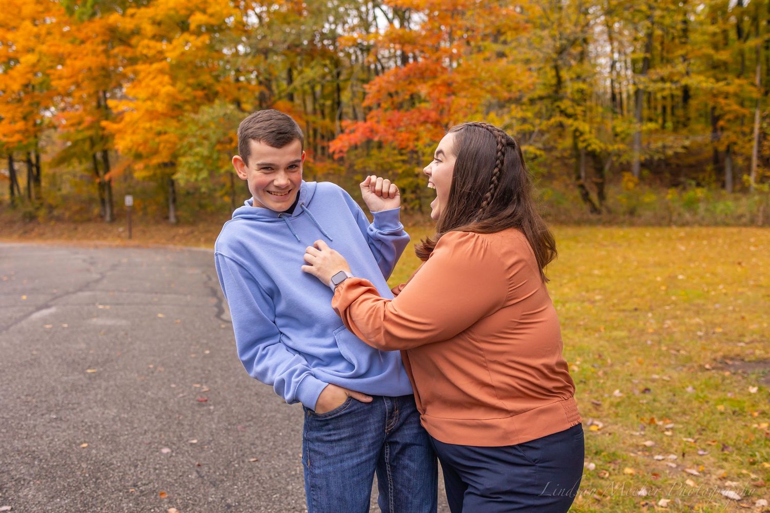 Two people share a playful moment outdoors surrounded by vibrant autumn foliage.