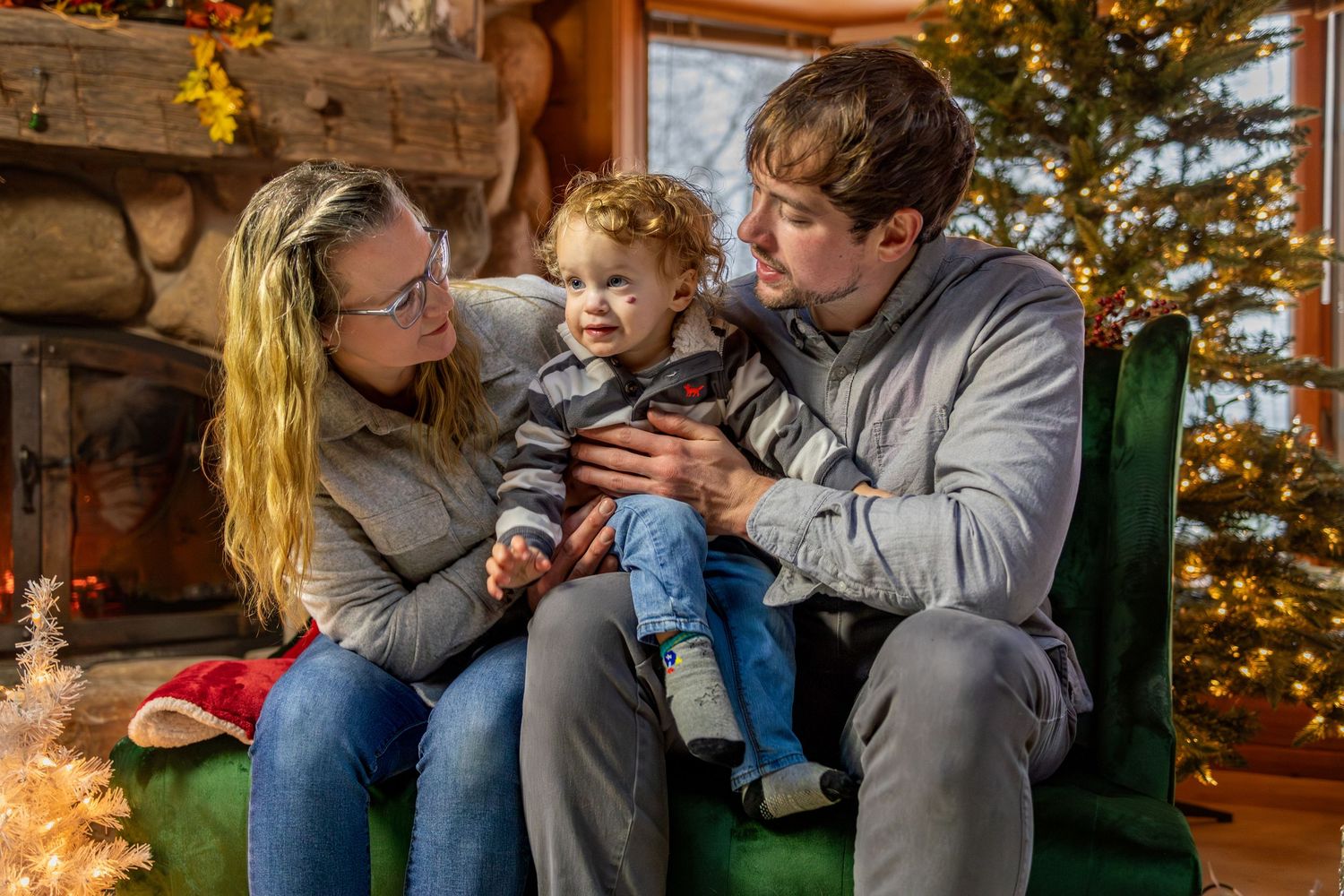 Family sits together on couch while decorating for Christmas near illuminated tree during a cozy holiday evening.