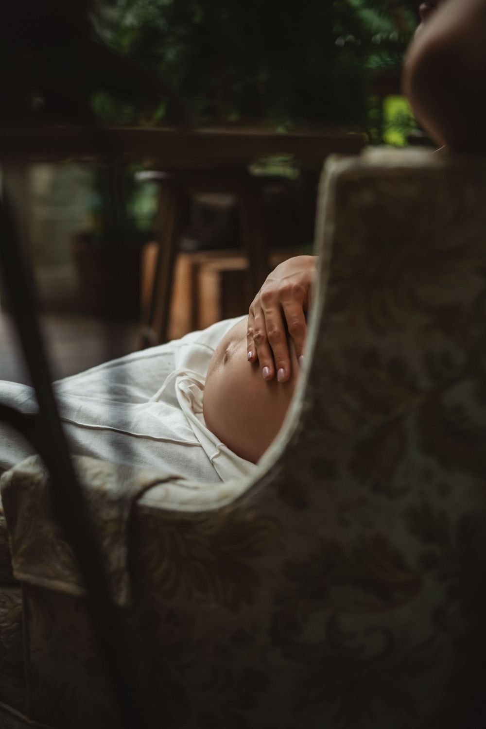 mom rests on a chair with only her hand over her bare pregnant belly visable