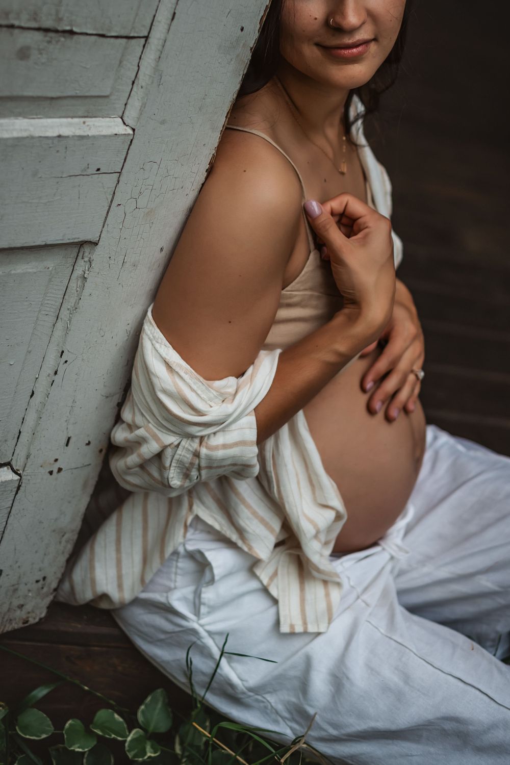 pregnant woman in linen two piece outfit lets her jacket slide off her bare shoulder as she hugs her exposed belly