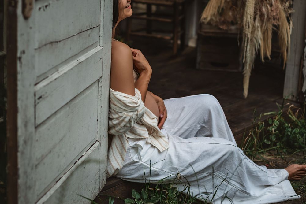 pregnant woman rests against the doorframe of a backyard greenhouse showing off her bare belly