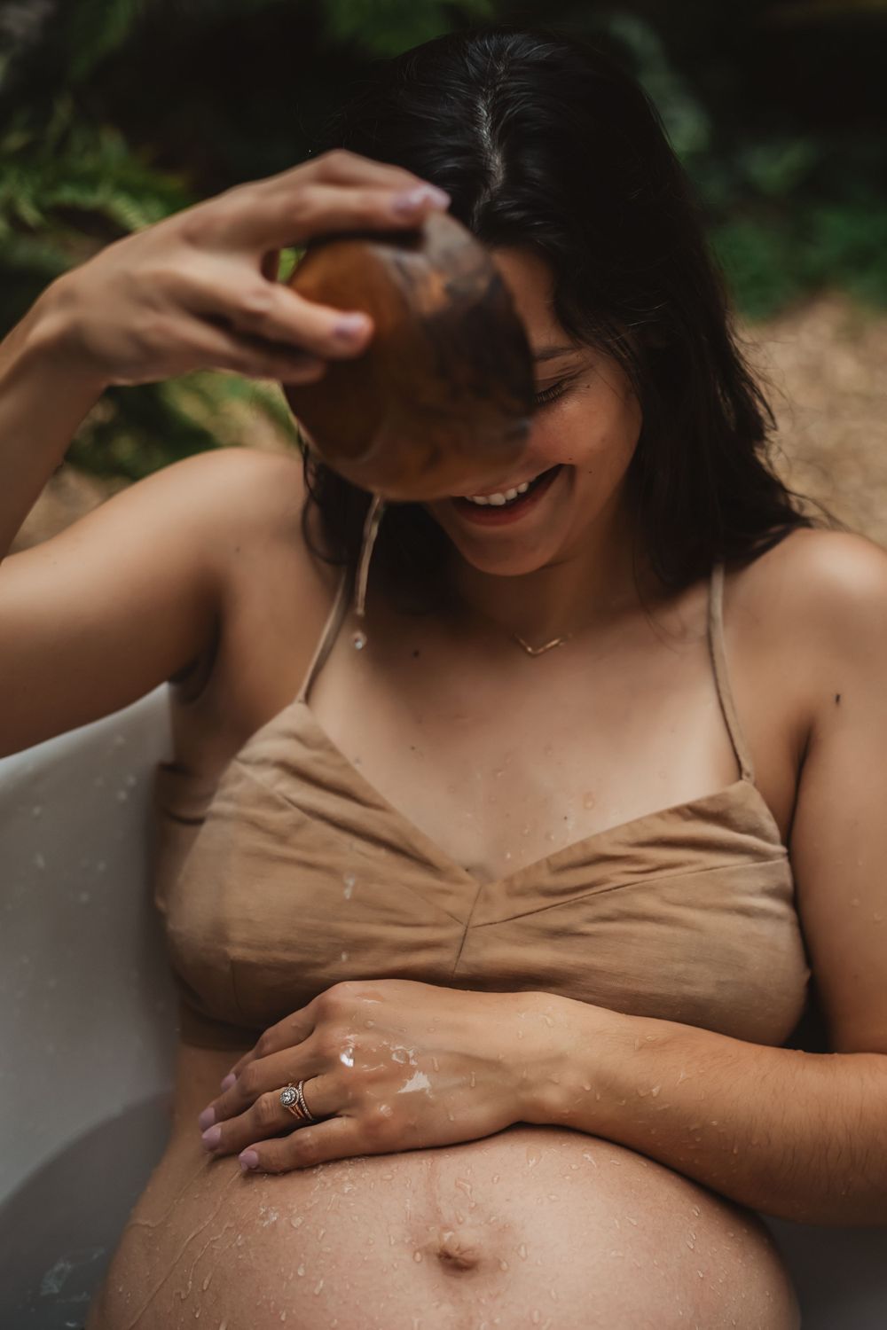 woman smiles and drips water onto bare pregnant belly for backyard bathtub maternity session