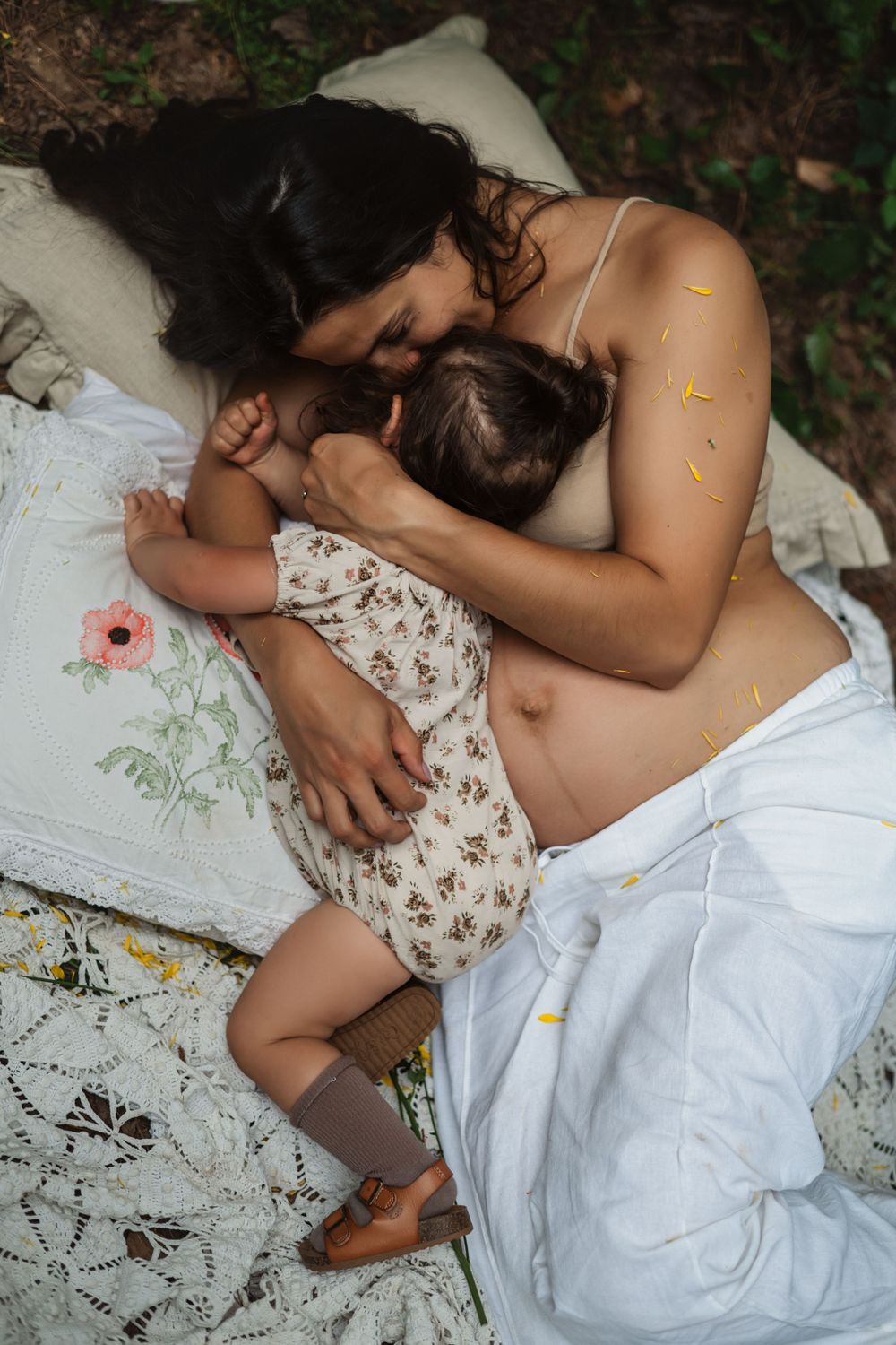 pregnant mother hugs her toddler daughter as they lie snuggling on a blanket under a clothesline