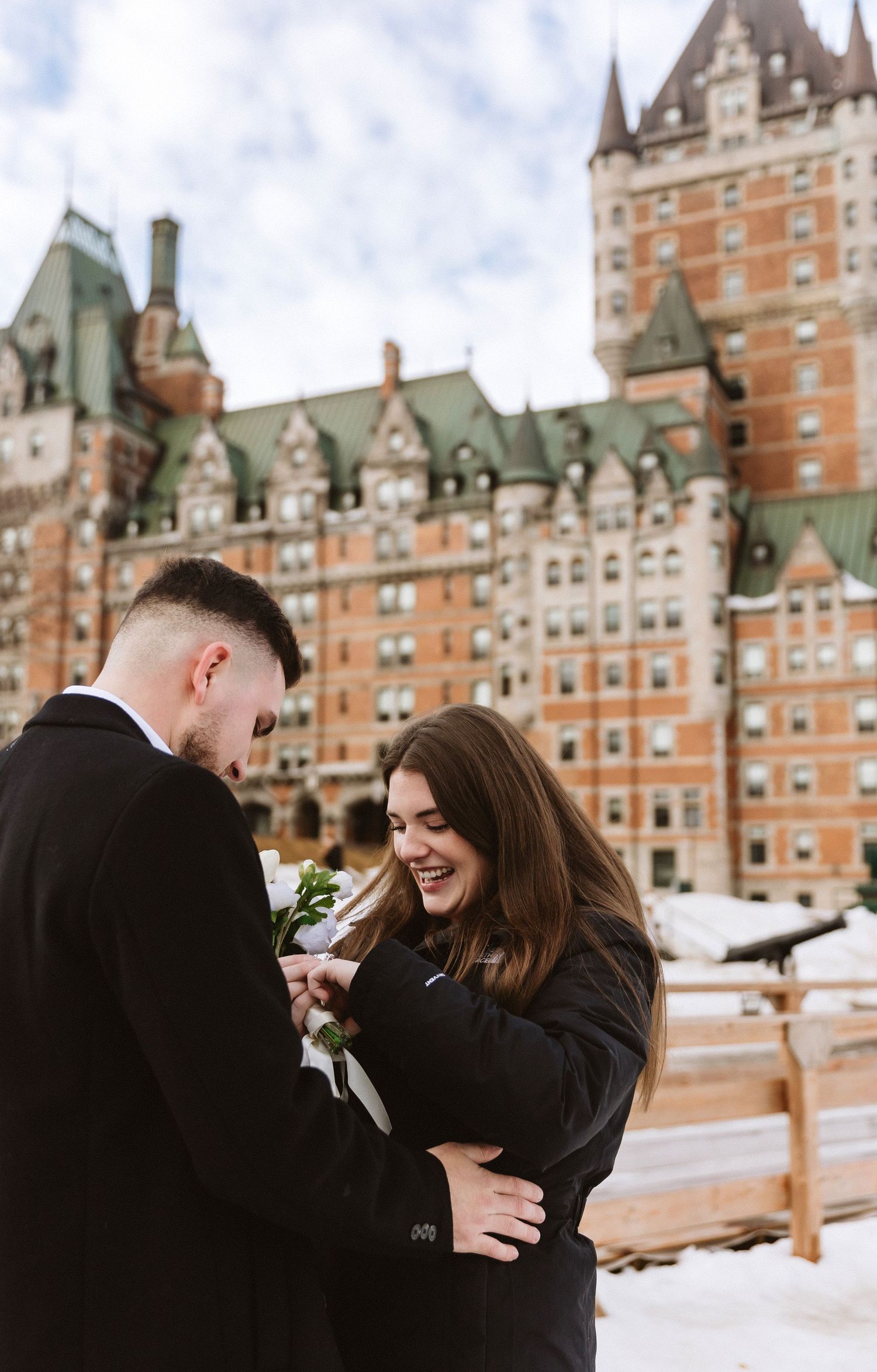Engagement moment captured in front of Chateau Frontenac during winter with snow on ground.