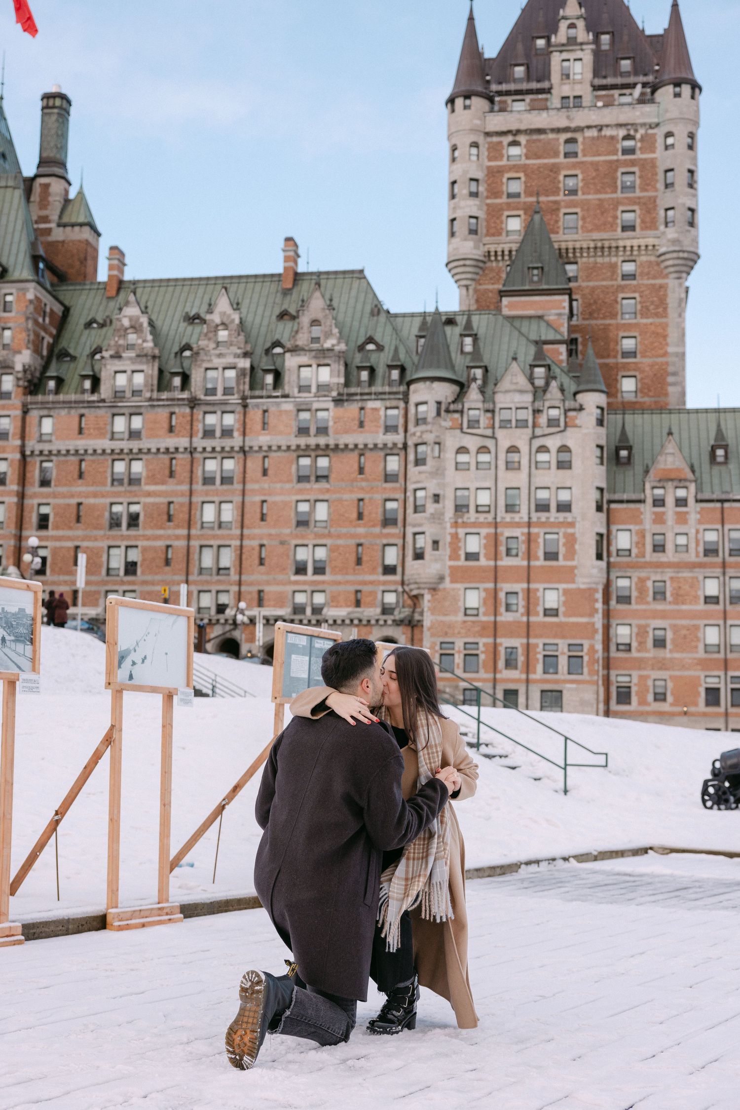 Scenic backdrop of Quebec City's Chateau Frontenac as a proposal takes place on a grassy hilltop overlooking the cityscape.