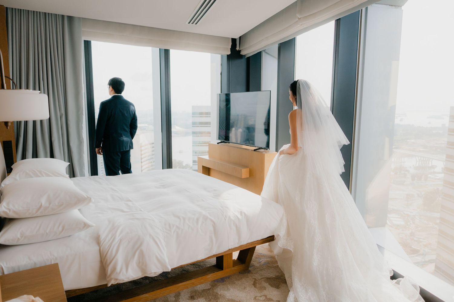 A bright contemporary hotel room with floor-to-ceiling windows overlooking a city skyline.