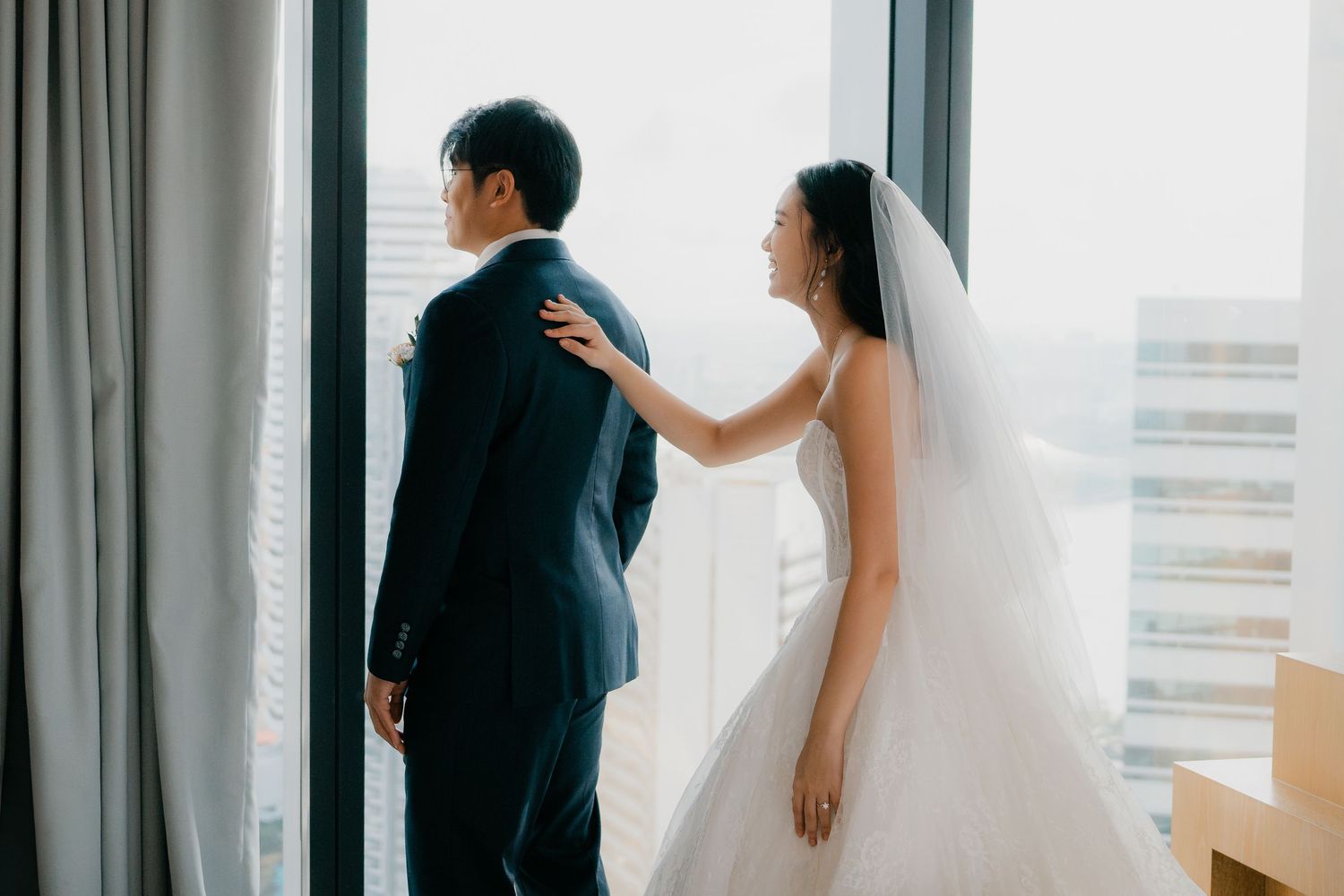 A bride and groom share a tender moment by a window during their wedding photo session.