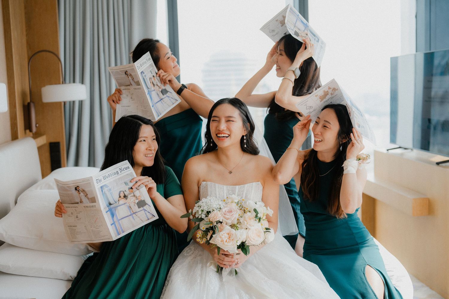 Wedding party members laugh and smile while looking at papers in a bright modern room.