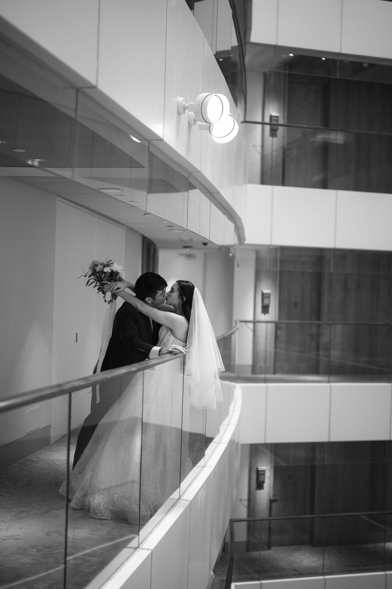 A black and white photo captures a romantic moment between newlyweds on a modern curved balcony.