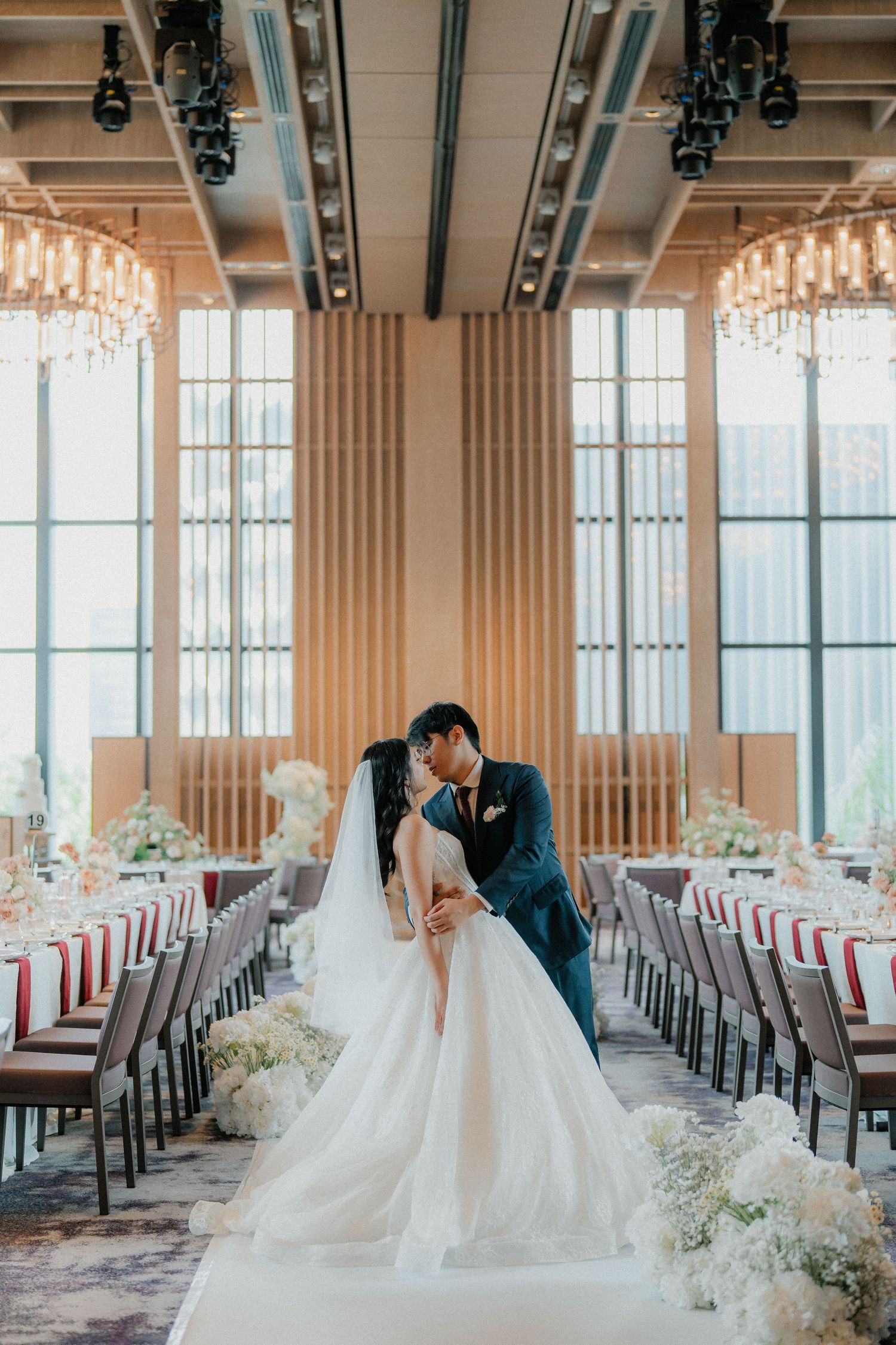 A romantic moment in an elegant wedding reception venue with crystal chandeliers and lined chairs.