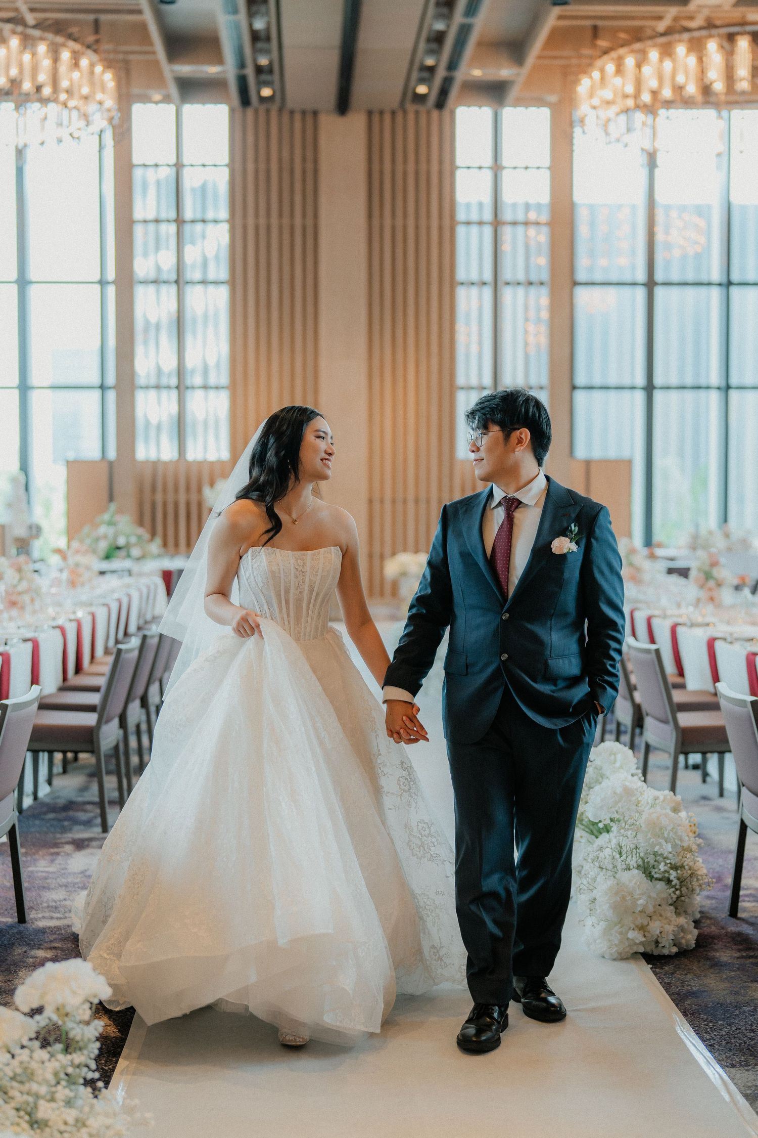 Newlyweds walking together in an elegant reception venue with floor-to-ceiling windows.
