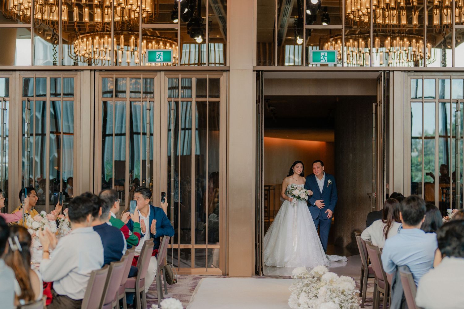 Wedding ceremony in an elegant ballroom with crystal chandeliers and glass panels.