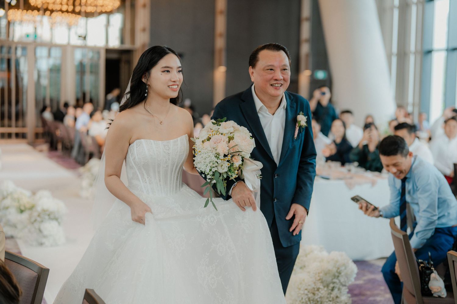 Wedding celebration in a modern banquet hall with large windows and festive table settings.