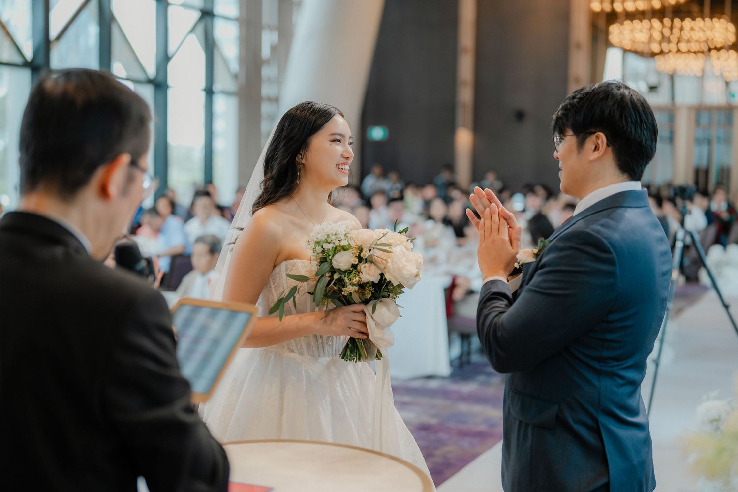 Bride holding bouquet shares joyful moment during wedding ceremony in elegant venue.