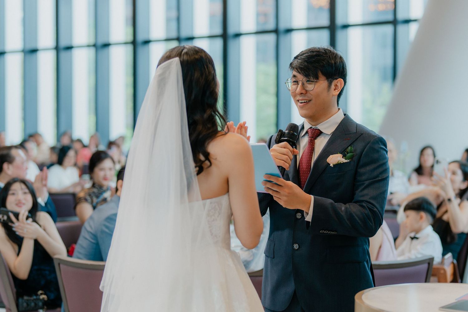 A bride and groom share a lighthearted moment during their wedding ceremony in a bright sunlit venue.