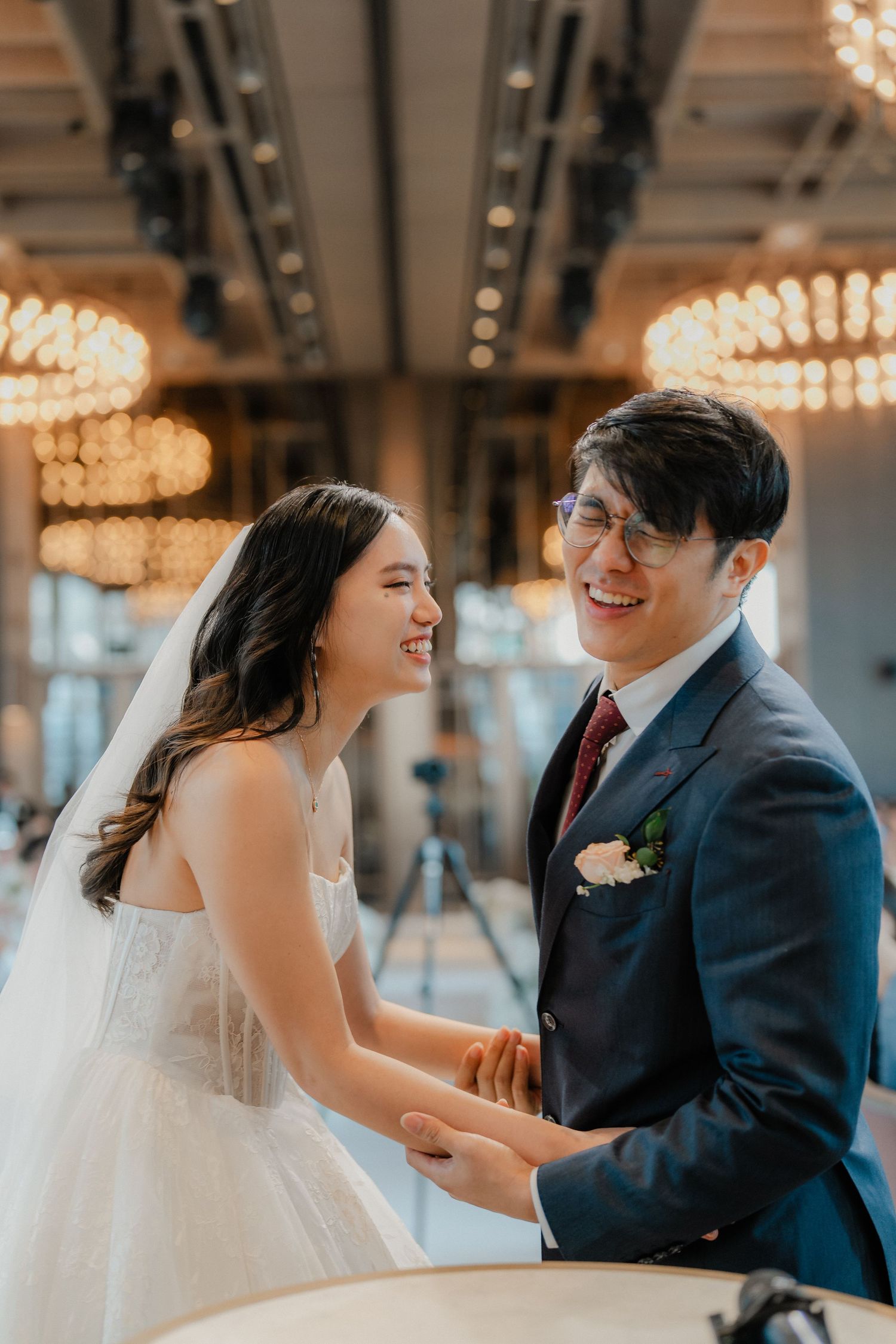 Happy couple sharing a candid moment during wedding reception under crystal chandeliers.