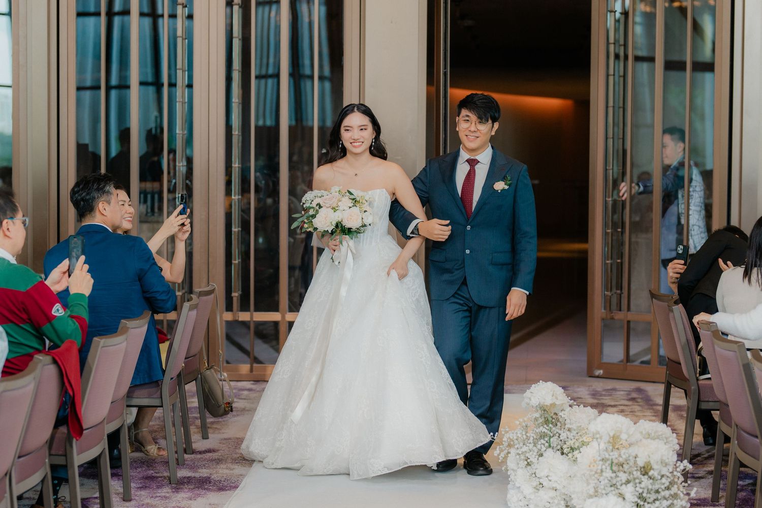 Couple making grand entrance into modern wedding reception hall with floral decorations.