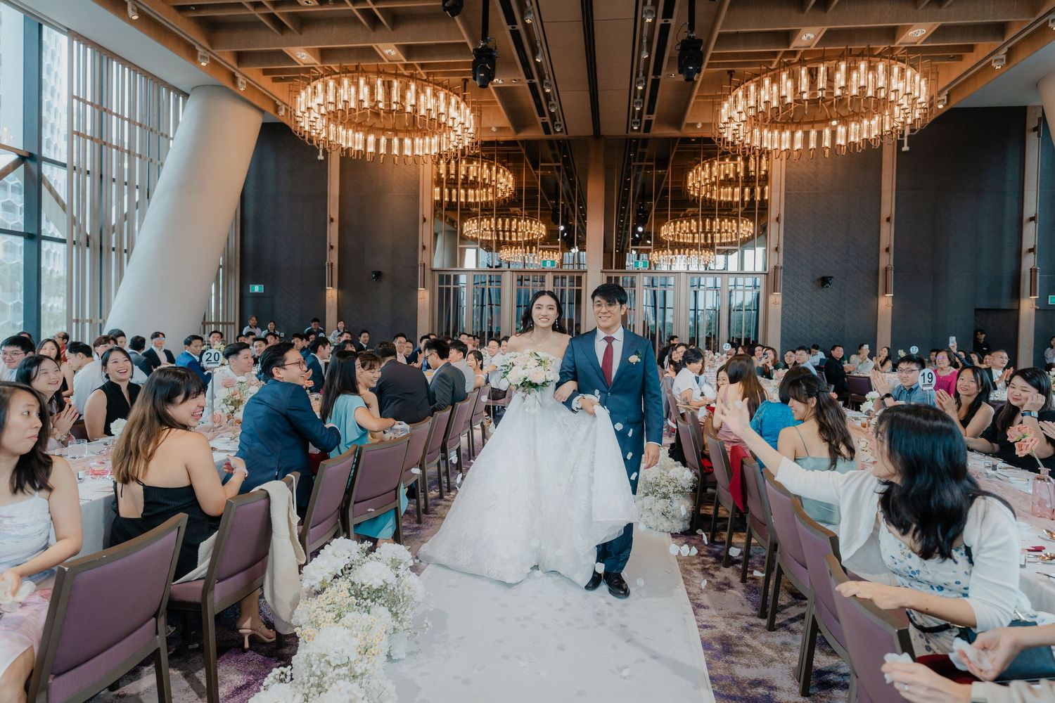 Newlyweds make their way through reception hall as guests look on.