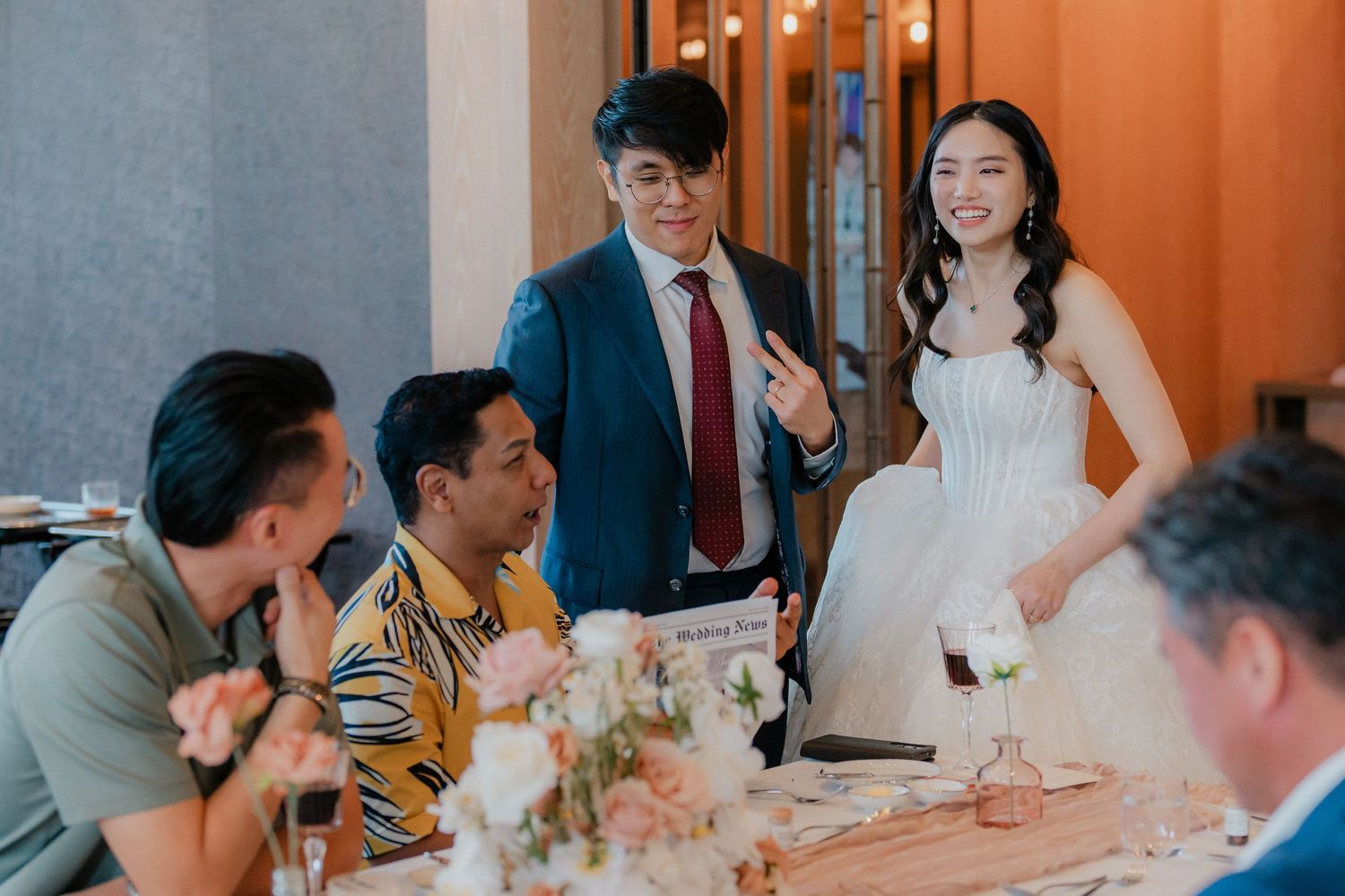 Wedding couple interacts with guests at a reception table decorated with elegant floral arrangements.