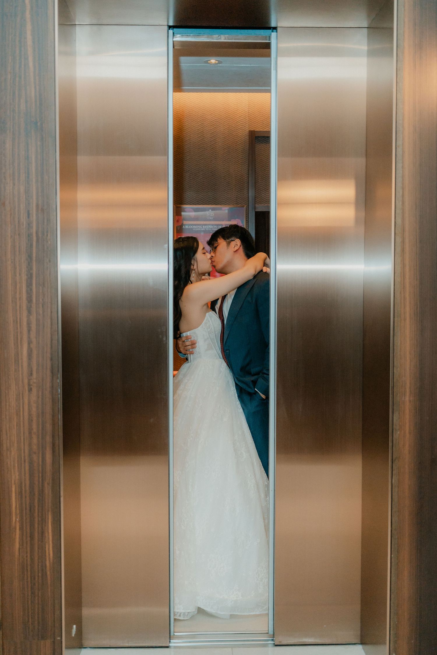Wedding couple sharing intimate moments through elevator panel reflections in modern stainless steel interior.