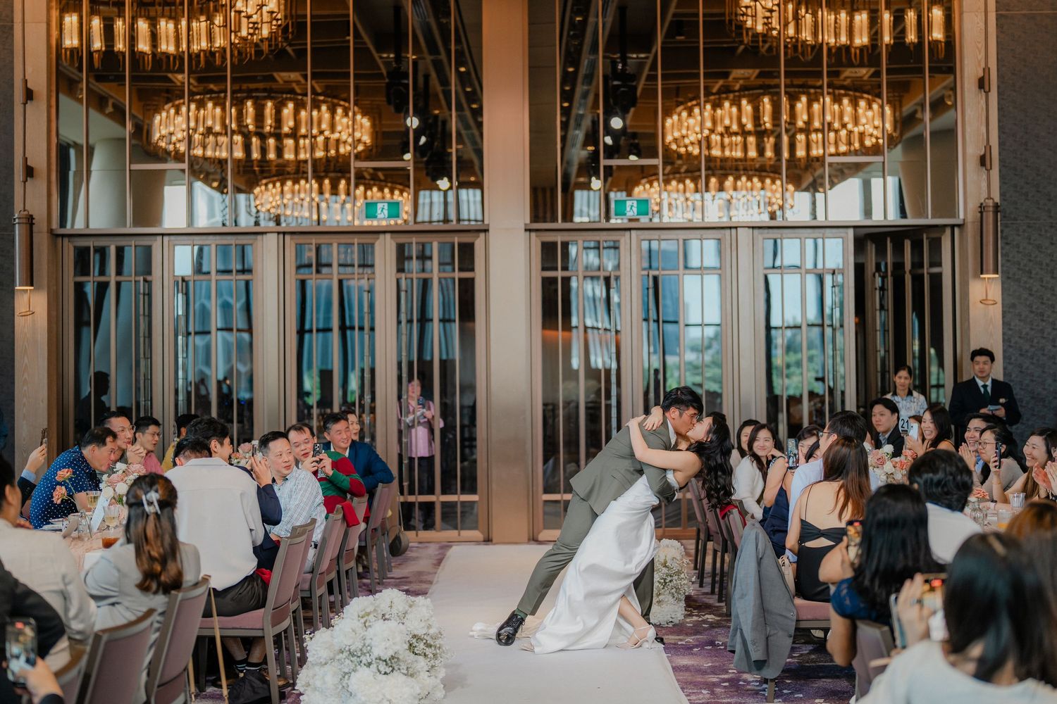 A couple executes a dramatic dance dip in a luxurious reception hall with sparkling chandeliers overhead.