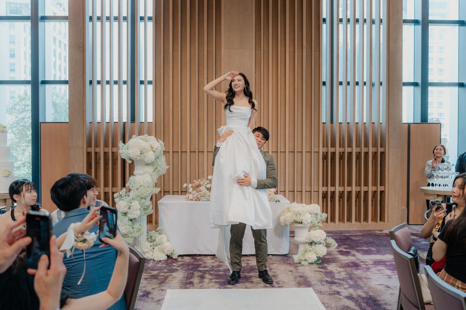 Wedding celebration with guests applauding in a modern venue with wood paneled walls.