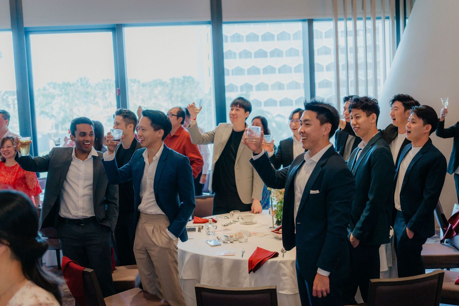 A celebratory group of guests in formal attire raise their glasses in a toast at an indoor event space.
