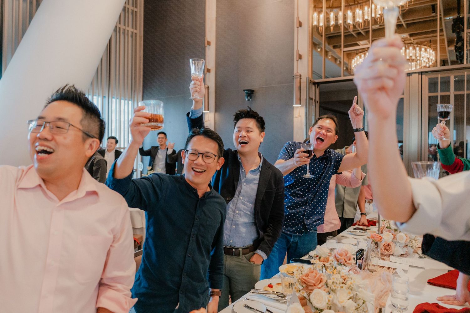Guests in formal attire raise their glasses in celebration at an elegant indoor banquet.