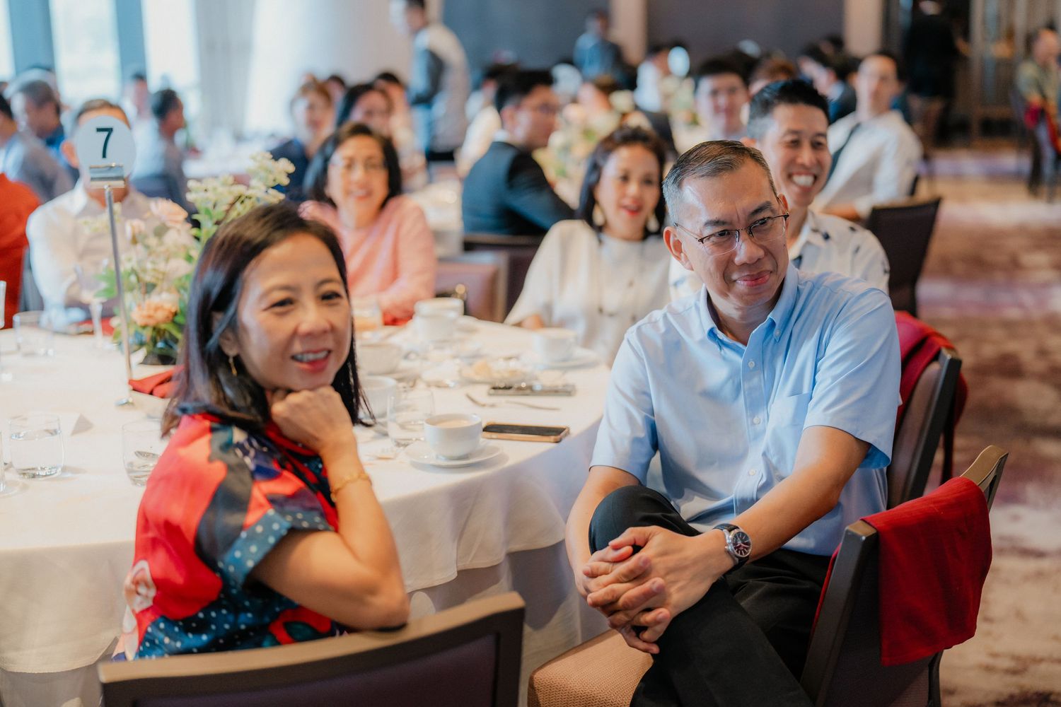 Wedding guests laugh and smile while seated at reception tables during a joyful celebration.