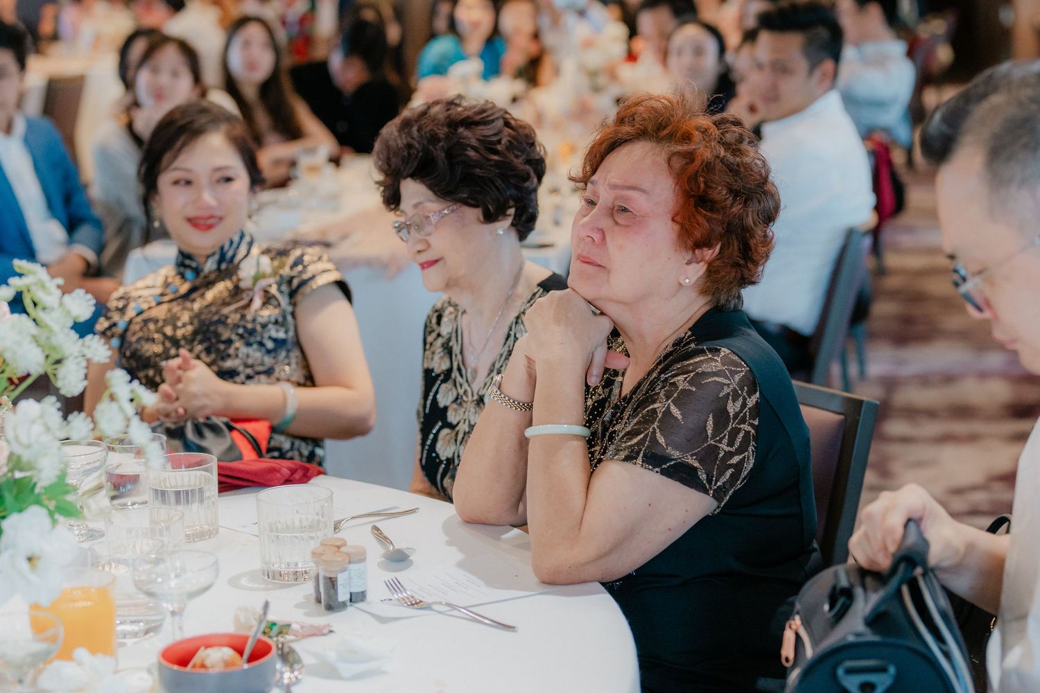 Wedding reception guests seated at round tables enjoying a celebratory meal in an elegant banquet hall.